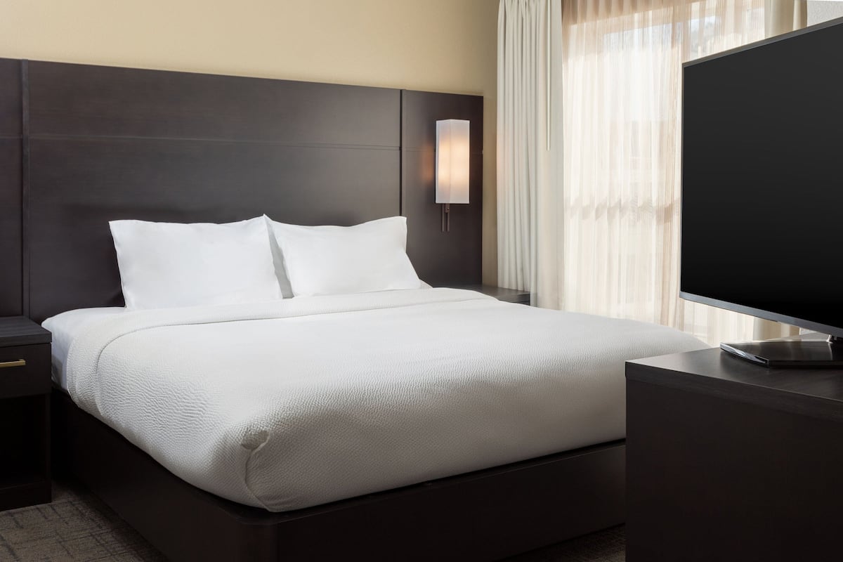 A modern hotel room with a large bed, a flat-screen TV, and a nightstand.
