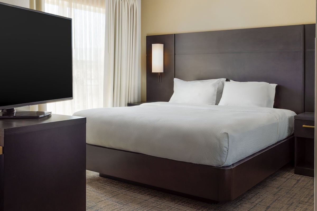A hotel room with a large bed, a flat-screen TV, a nightstand, and a wall-mounted light.