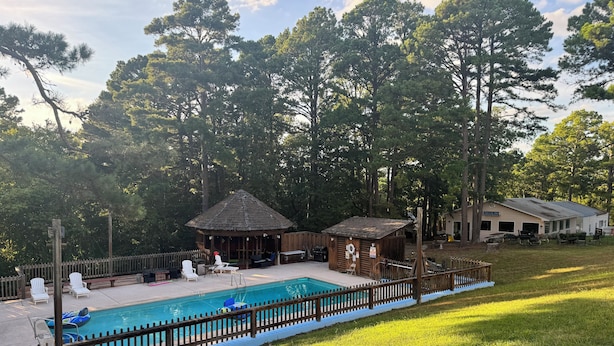 Un espace piscine avec des chaises longues, une petite structure en bois et une terrasse délimitée par une clôture.