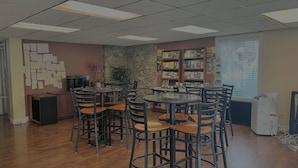 Une bibliothèque dotée de plusieurs tables et chaises, d’étagères, d’un mur en pierre et d’une fenêtre avec des stores.