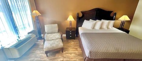Ein Hotelzimmer mit einem Bett, einem Sessel, zwei Nachttischen mit Lampen, einem Heizkörper und einem Fenster mit Vorhängen.