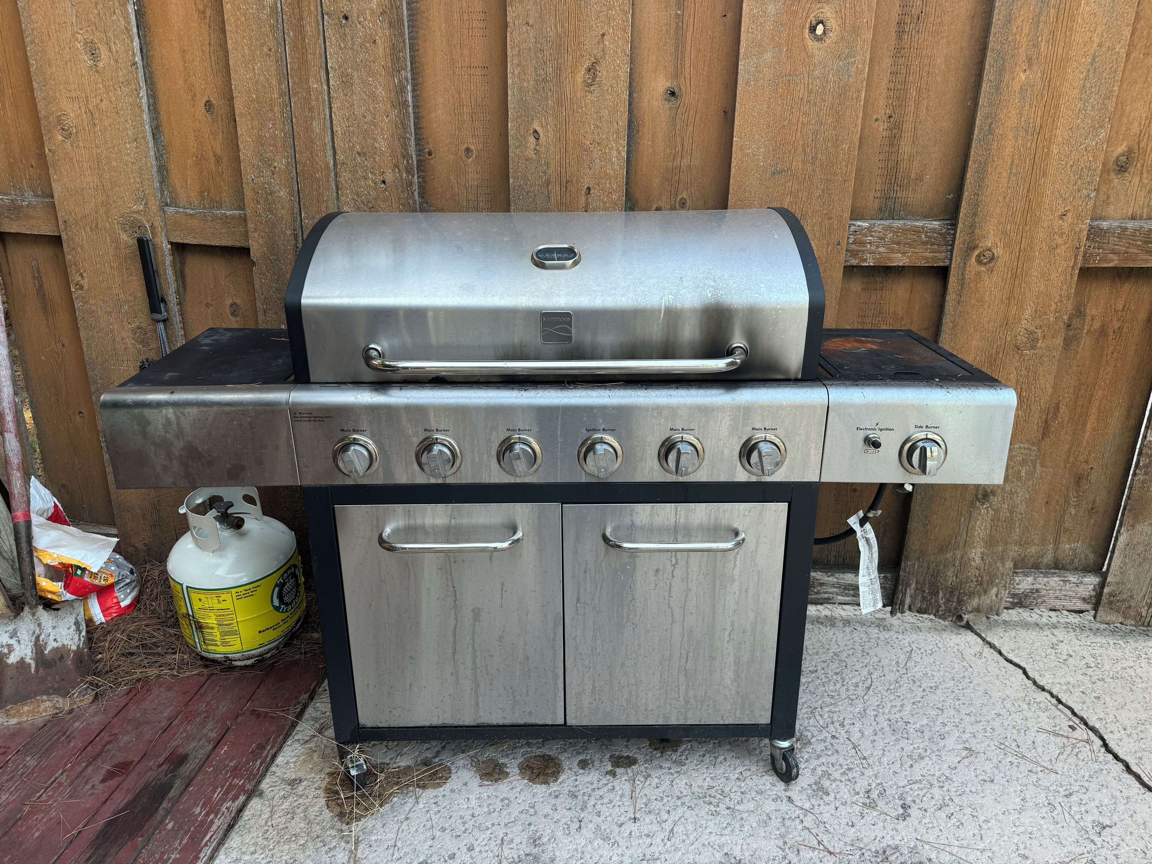 A stainless steel barbecue grill with a side burner and a gas tank.