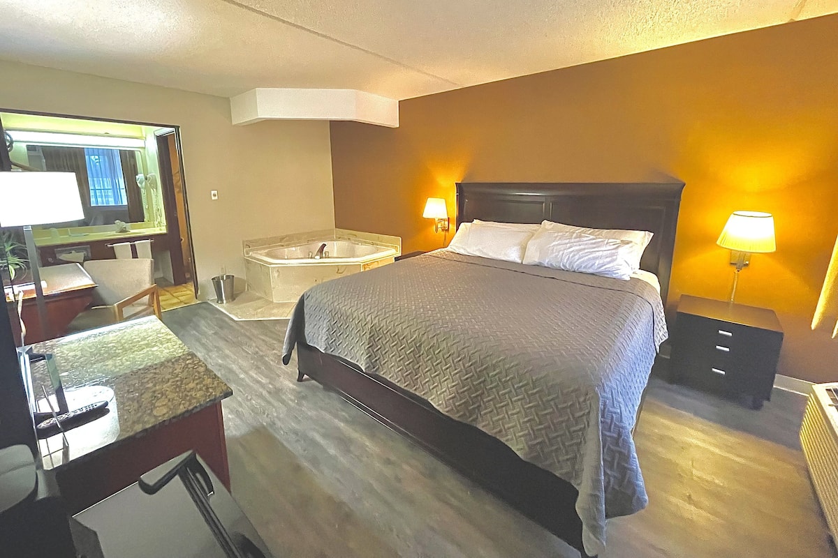 Habitación de hotel con una cama grande, un escritorio con una silla, un tocador con espejo y una bañera.