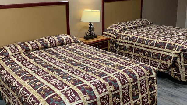 A hotel room with two beds, each with a patterned bedspread and a bedside table with a lamp. - Budget Inn San Gabriel (San Gabriel)