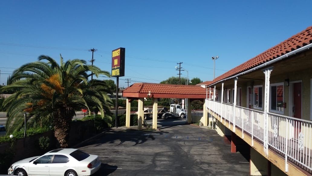 A motel with a covered parking area, a palm tree, and a white car parked in front.