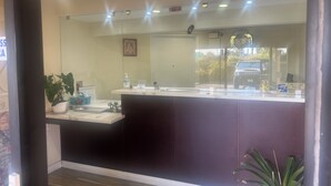 A reception area with a counter, a clock, and a sign indicating the availability of assistive devices. - Budget Inn San Gabriel (San Gabriel)