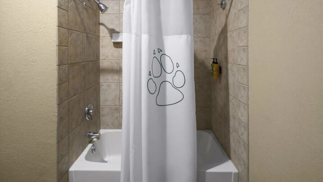 Un baño con cortina de ducha con diseño de huellas, un lavabo blanco y un cabezal de ducha de mano.