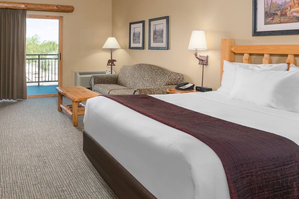 A hotel room with a large bed, a chair, a desk, and a balcony.