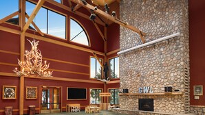 A spacious lobby with a stone fireplace, wooden beams, large windows, and a chandelier. - Great Wolf Lodge Wisconsin Dells (Baraboo)