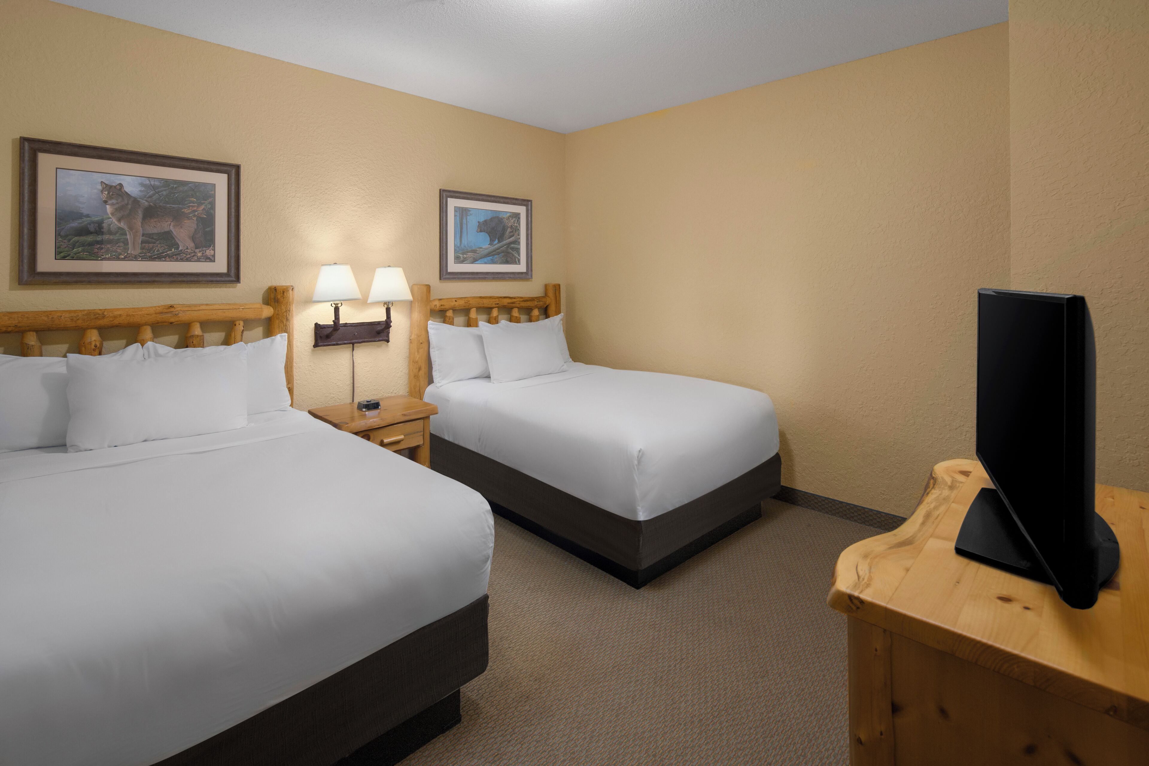 A hotel room with two beds, a TV on a wooden stand, and two framed pictures on the wall.