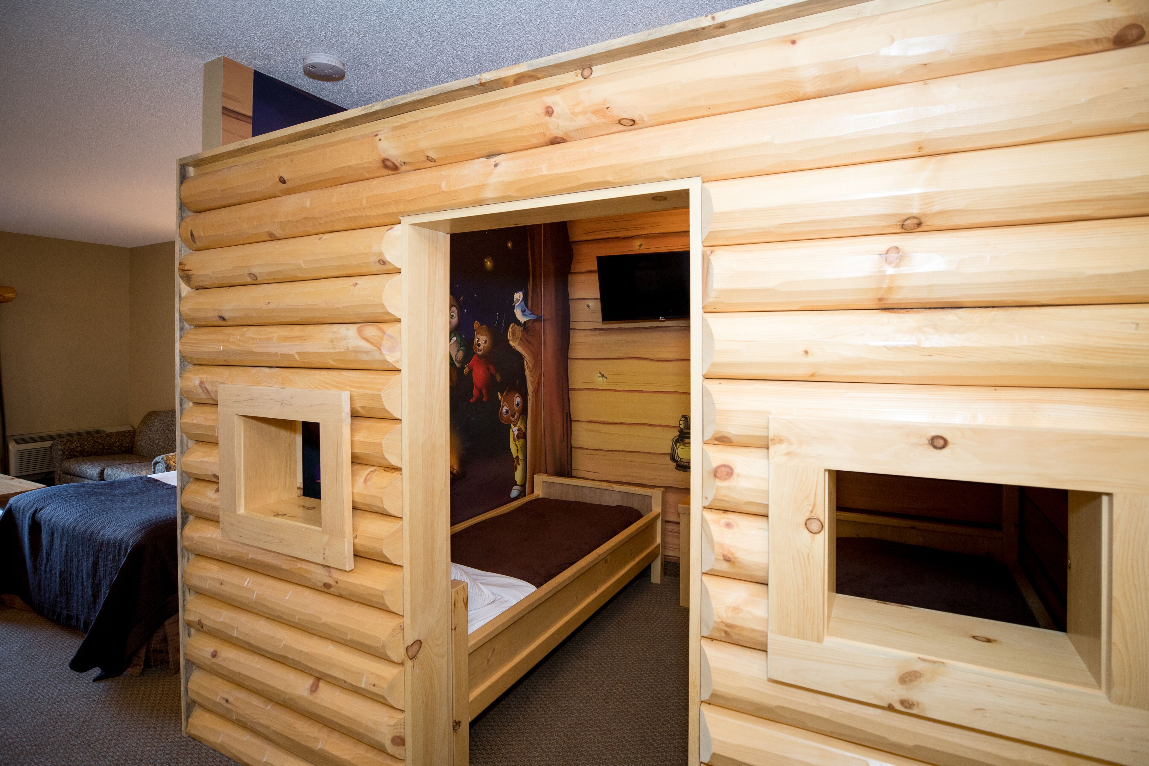 Une chambre de style cabane, avec une façade en bois, un lit simple, un petit bureau et un téléviseur.