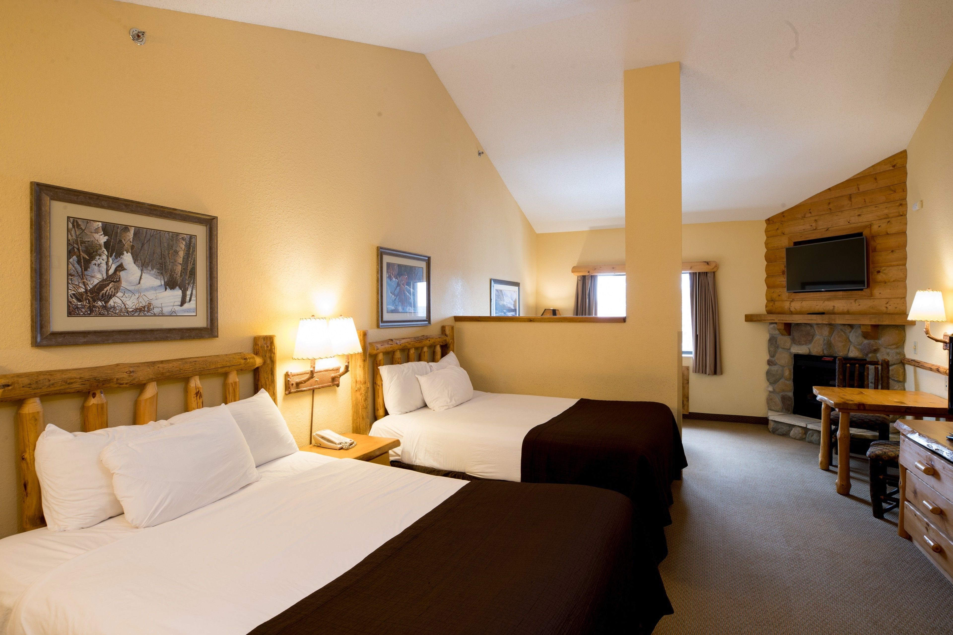 A hotel room with two beds, a fireplace, a television, and a dining area.