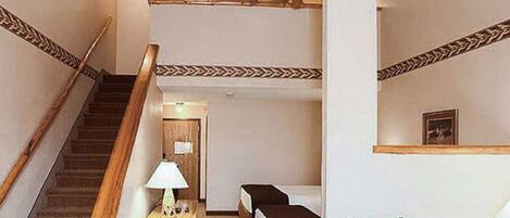 A staircase with wooden handrails, a ceiling fan, and a small table with a lamp.