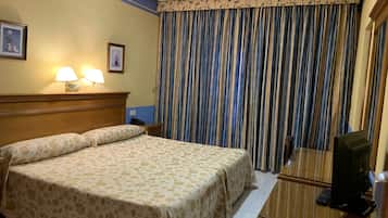 Une chambre d’hôtel avec un lit, des lampes de chevet, un bureau avec un ordinateur et une grande fenêtre avec des rideaux à rayures.