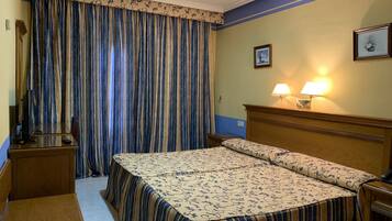Ein Hotelzimmer mit Bett, Schreibtisch, Stuhl, Lampe und Vorhängen.