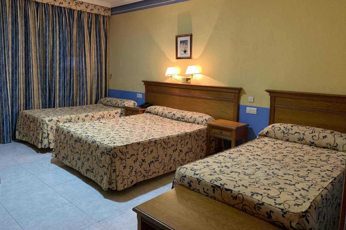 A hotel room with two beds, a nightstand, a lamp, and a framed picture on the wall.
