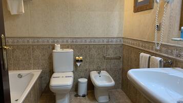 Een badkamer met toilet, bidet, prullenbak en een bad.