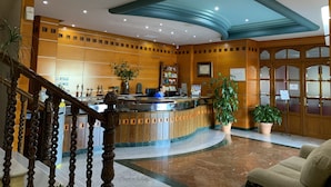Eine Hotelhalle mit Empfangstresen, Holzvertäfelung, Marmorböden und einer Treppe.