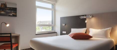 Une chambre d’hôtel avec un grand lit, un bureau, une chaise, une fenêtre et un tableau au mur.