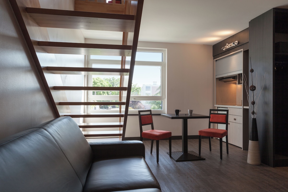 Un salon moderne comprenant un canapé, une table à manger avec des chaises, une fenêtre avec des stores et un escalier.