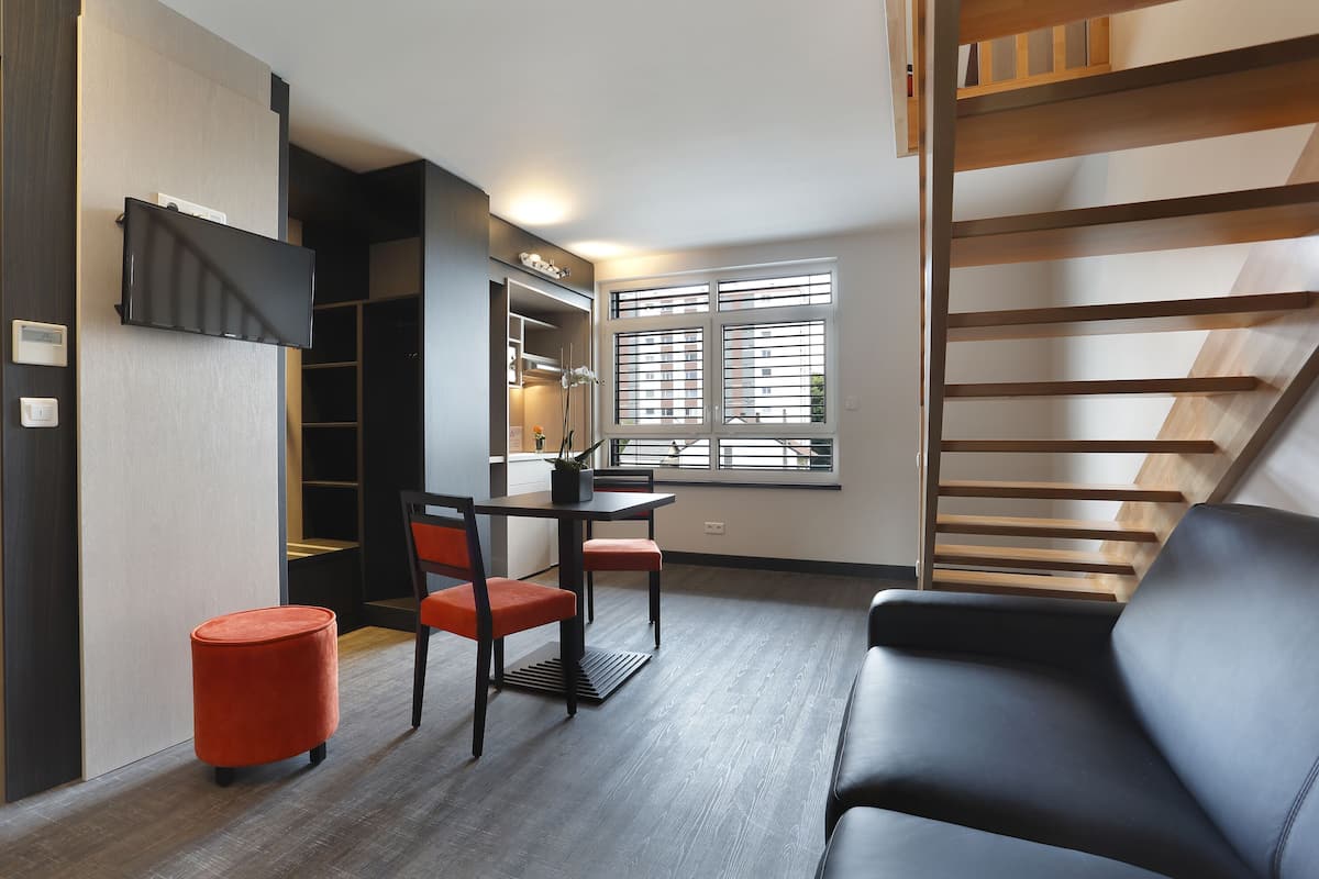 Un salon moderne avec un canapé noir, une table à manger avec des chaises et un escalier.