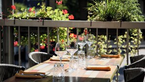 A dining table set with wine glasses and a menu, surrounded by wicker chairs, with a railing and greenery in the background. - The Originals Boutique, Hôtel d'Alsace, Strasbourg Sud (Illkirch-Graffenstaden)