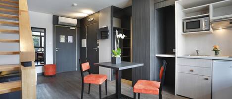 Una cocina moderna con microondas, un lavabo y una pequeña encimera. Hay una mesa de comedor con dos sillas y una planta en maceta.
