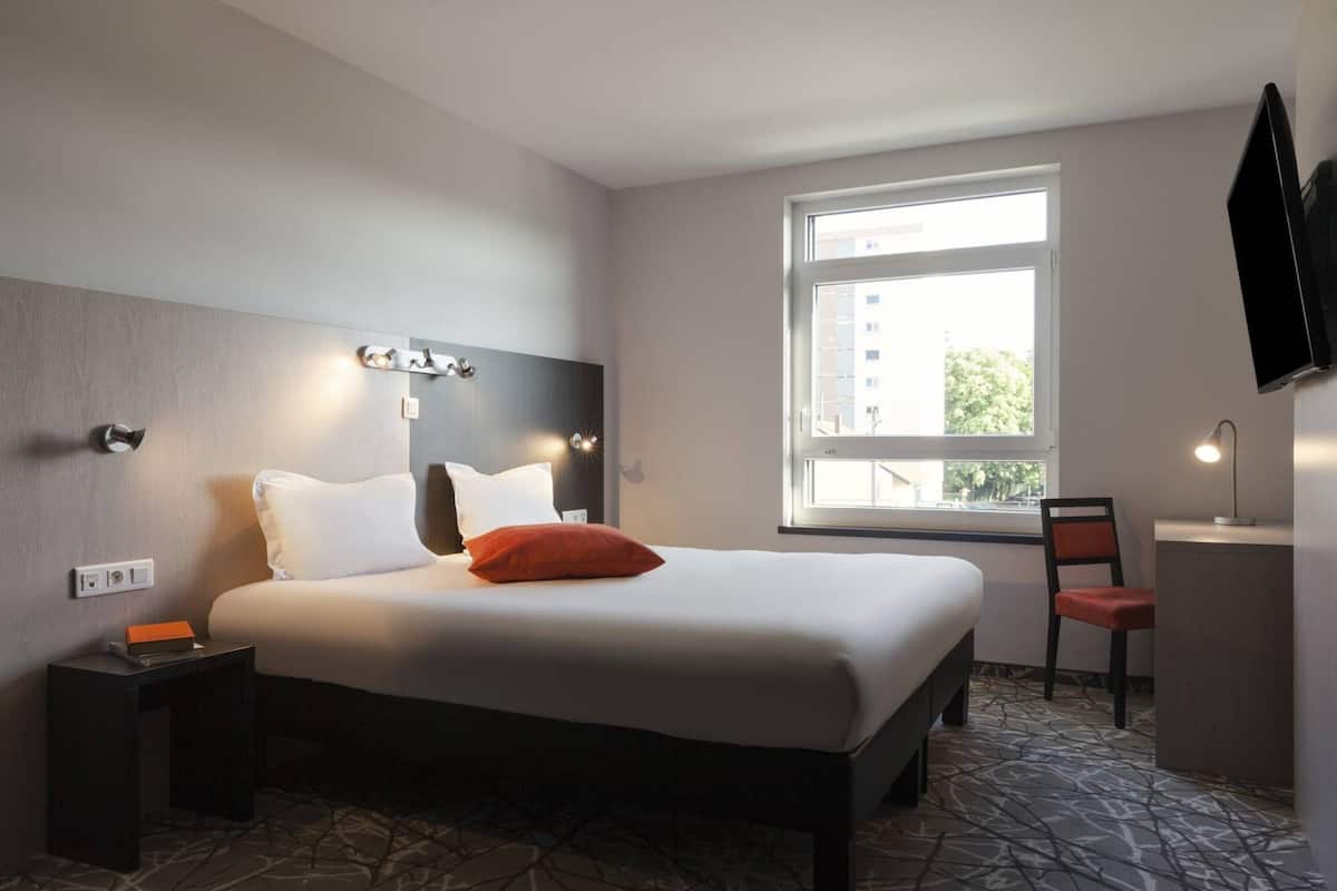 Une chambre d’hôtel comprenant un lit, une table de chevet, une chaise, un bureau et un téléviseur.