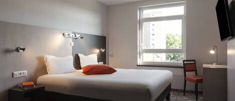 Hotelkamer met een bed, bureau, stoel, televisie en raam met uitzicht op gebouwen.