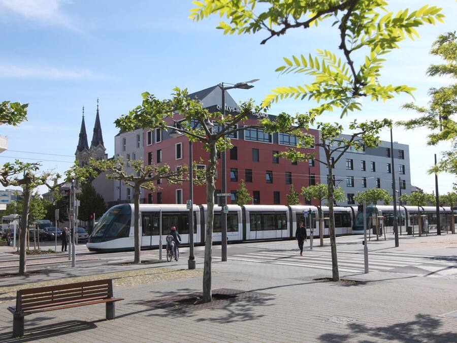 A modern urban setting with a tram, trees, and a bench.