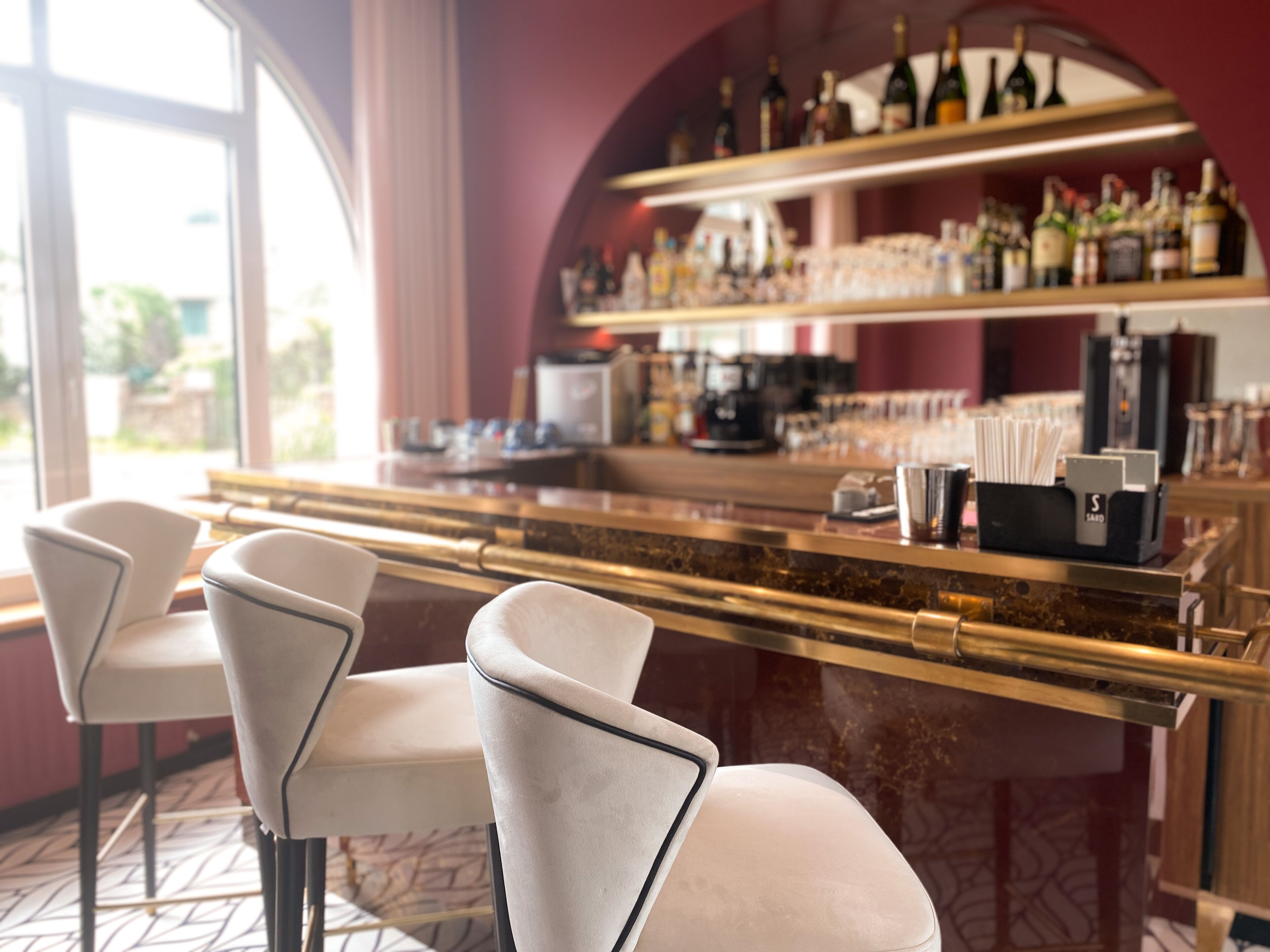 Un espace bar avec deux tabourets blancs, un comptoir avec une machine à café et des étagères remplies de bouteilles.