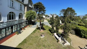 A courtyard with a glass conservatory, stone buildings, and a well-maintained garden with pathways and seating areas. - L'Escale Hôtel Bellevue (Tregastel)