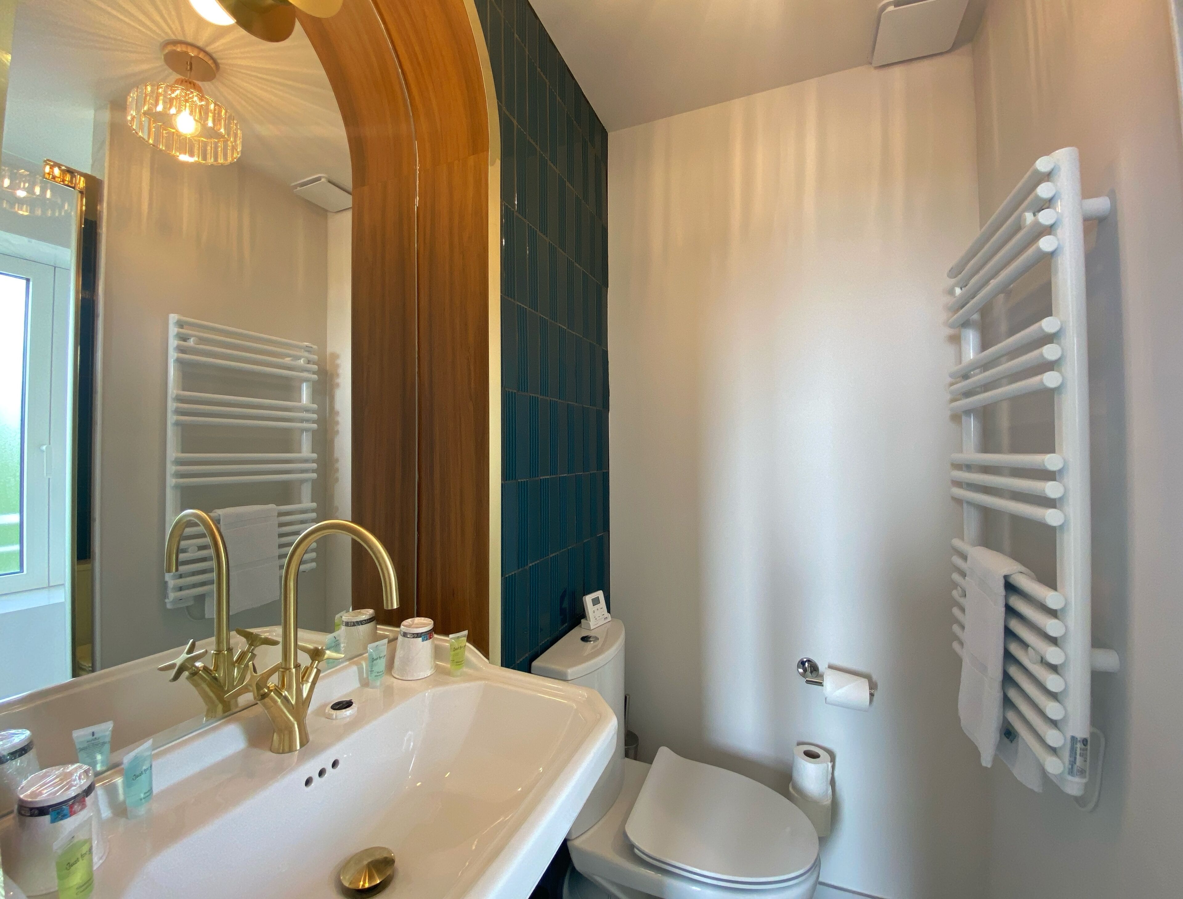 A bathroom with a white sink, gold faucets, a white toilet, and a towel rack.