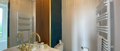 A bathroom with a white sink, gold faucets, a white toilet, and a towel rack.