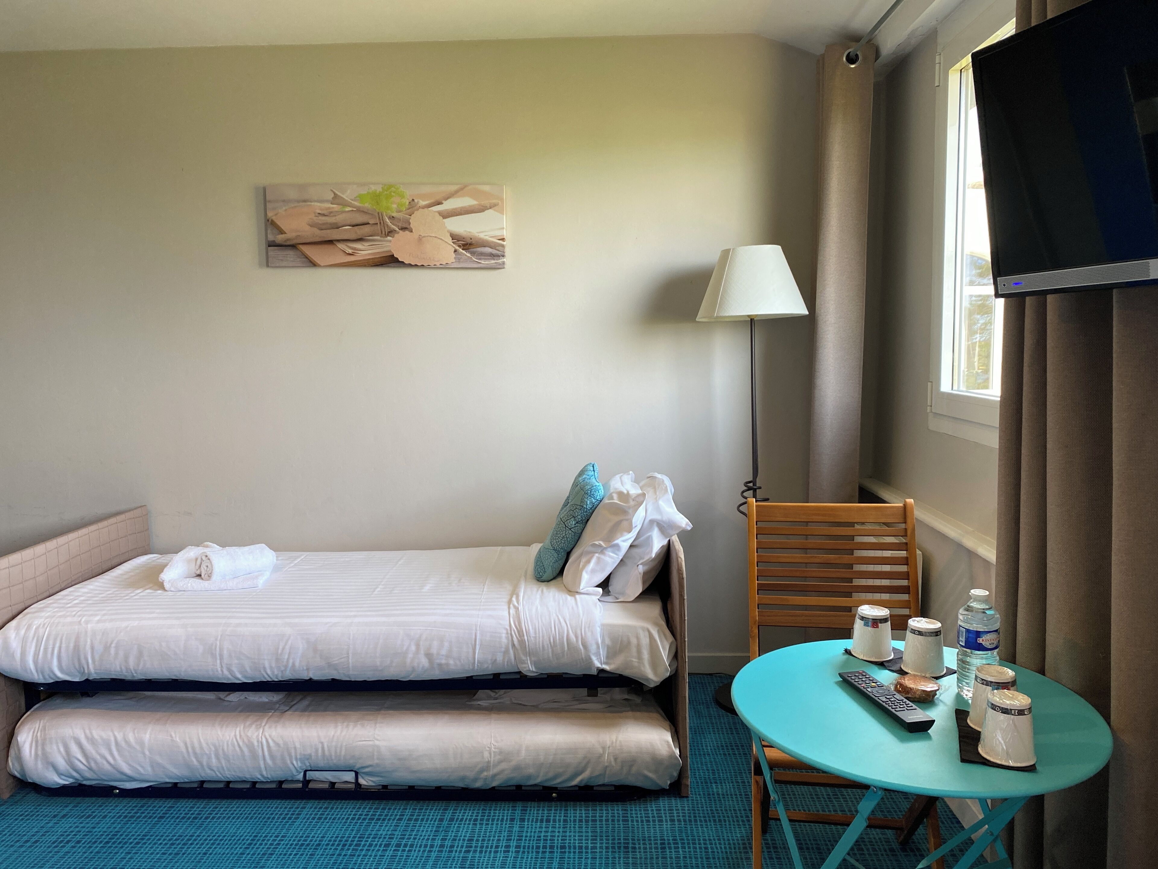 Une chambre d’hôtel avec un lit, une petite table sur laquelle sont posés quelques objets, une lampe et un téléviseur.