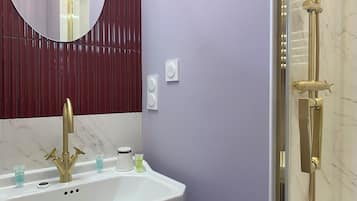 Une salle de bain avec un lavabo blanc, des robinets dorés, un miroir rond et une douche avec des accessoires dorés.