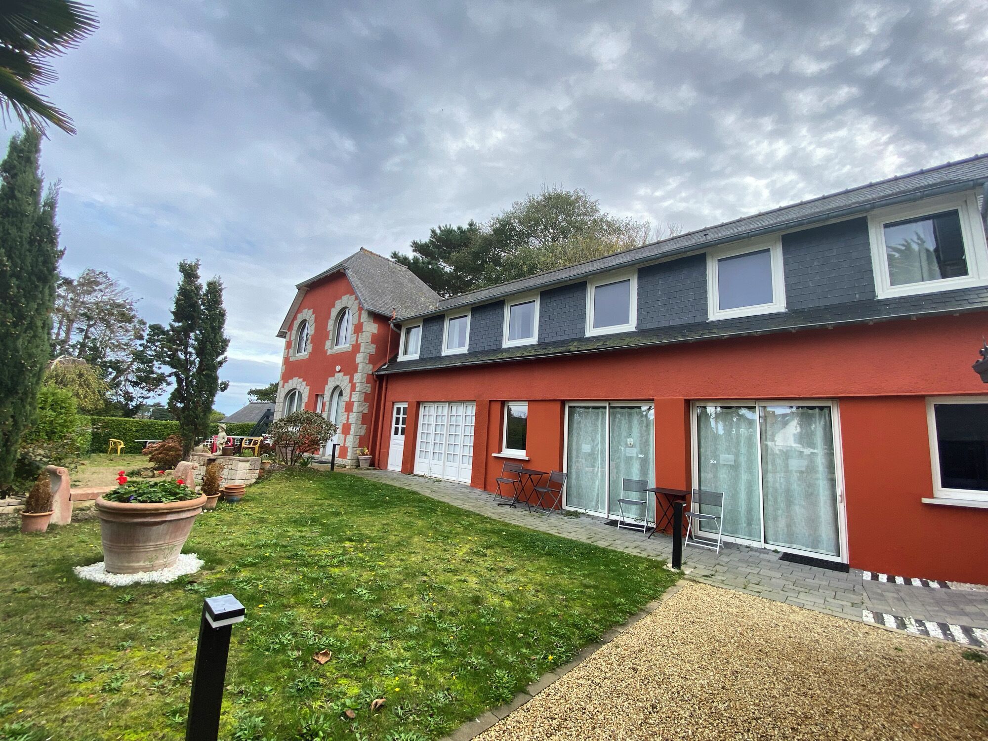 A red building with a large garage door, a well-maintained lawn, and a gravel pathway.