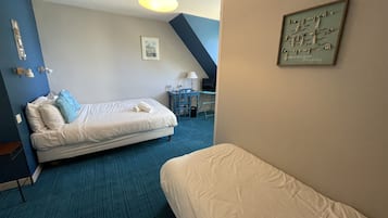 A hotel room with a bed, a desk, and a chair. There is a lamp on the desk and a framed quote on the wall.