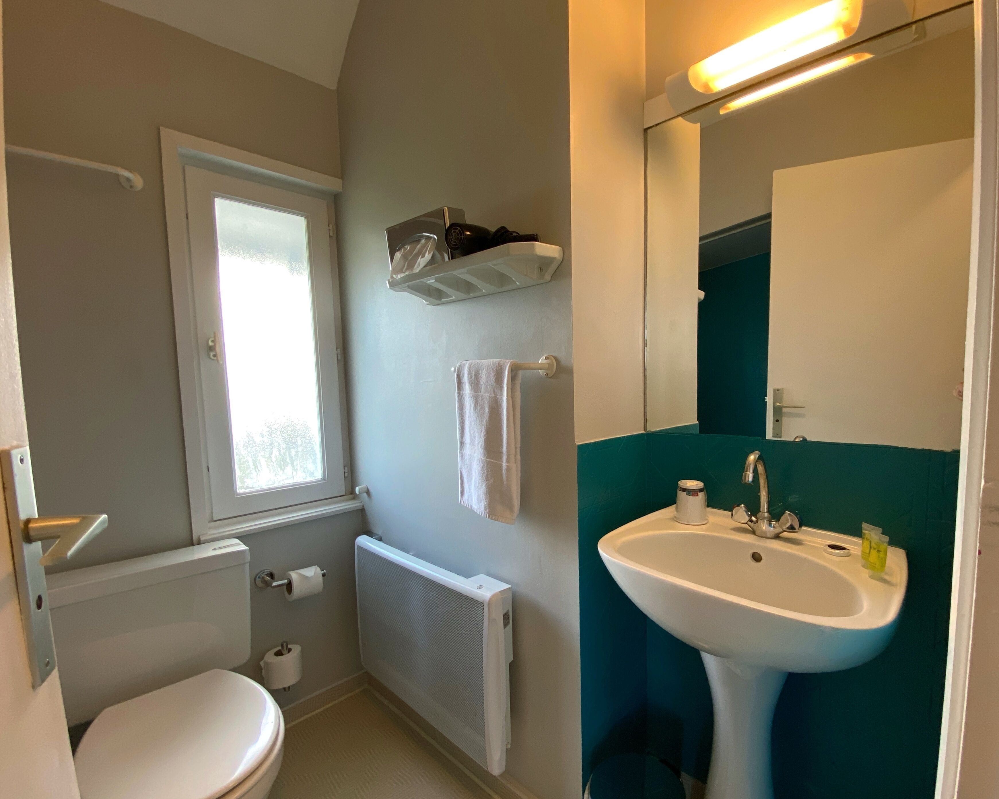Une salle de bain équipée de toilettes, d’un radiateur, d’un lavabo et d’une fenêtre.