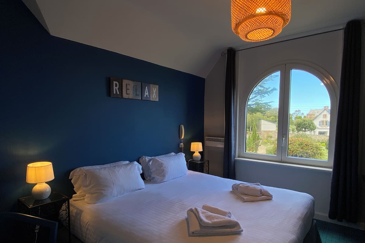 A hotel room with a large bed, two bedside lamps, a window with a view, and a 'RELAX' sign on the wall.