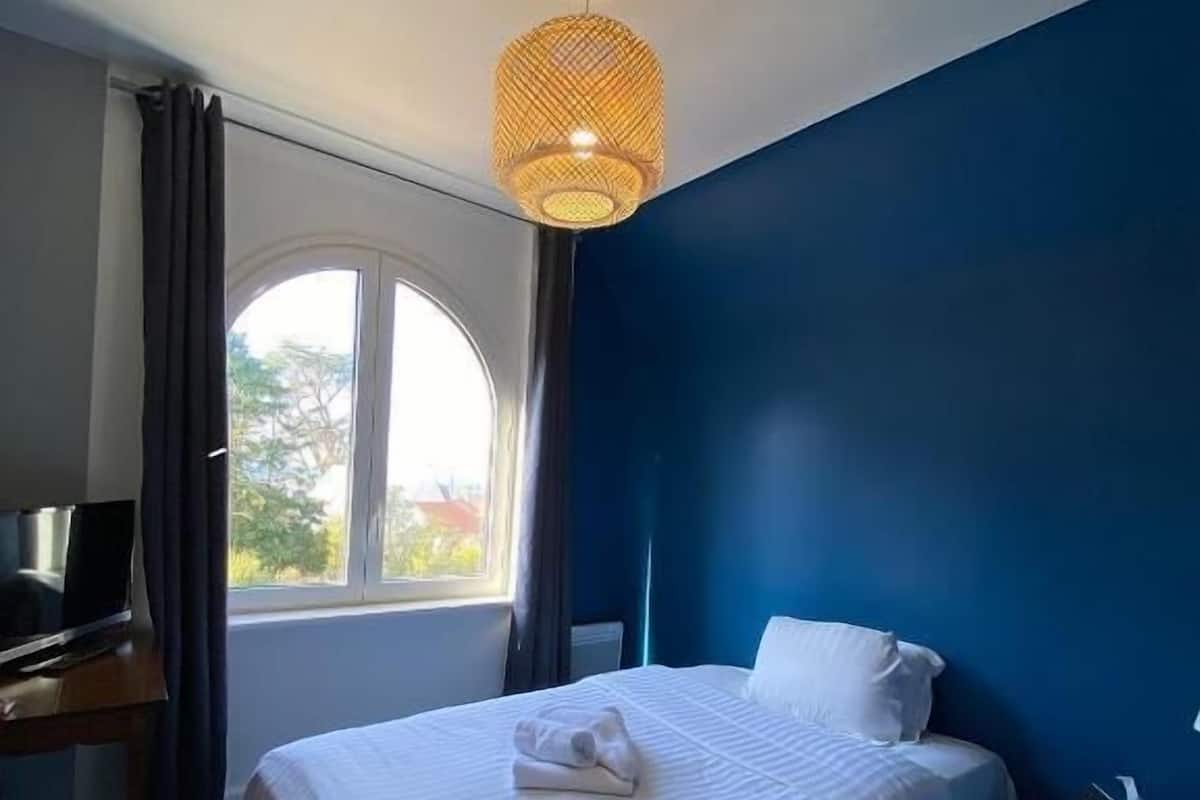 A hotel room with a bed, a desk, a television, and a window with curtains.