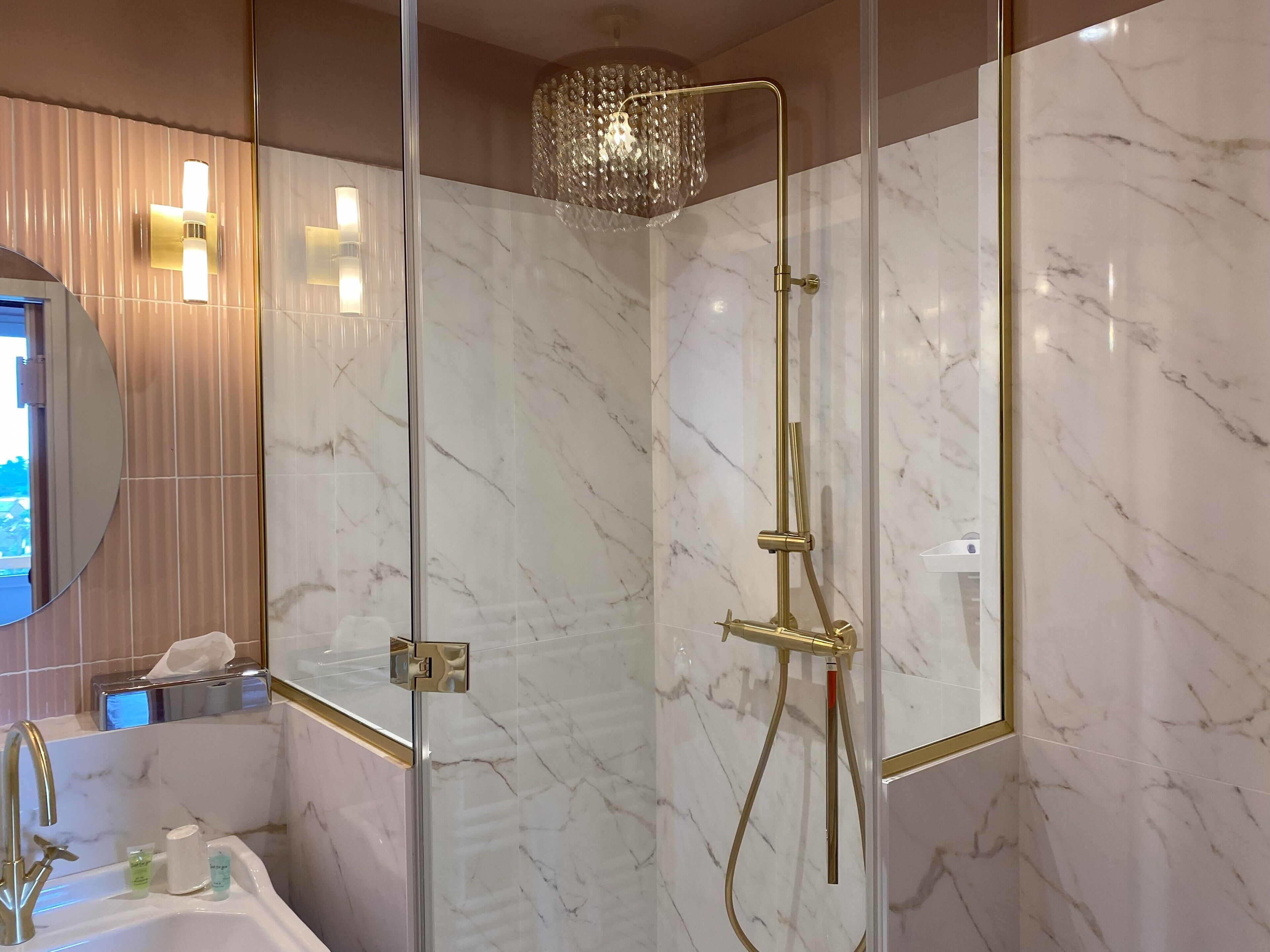 A modern bathroom with a glass-enclosed shower, marble walls, and a gold faucet.