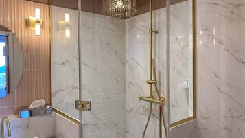 A modern bathroom with a glass-enclosed shower, marble walls, and a gold faucet.