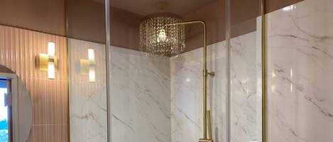 A modern bathroom with a glass-enclosed shower, marble walls, and a gold faucet.