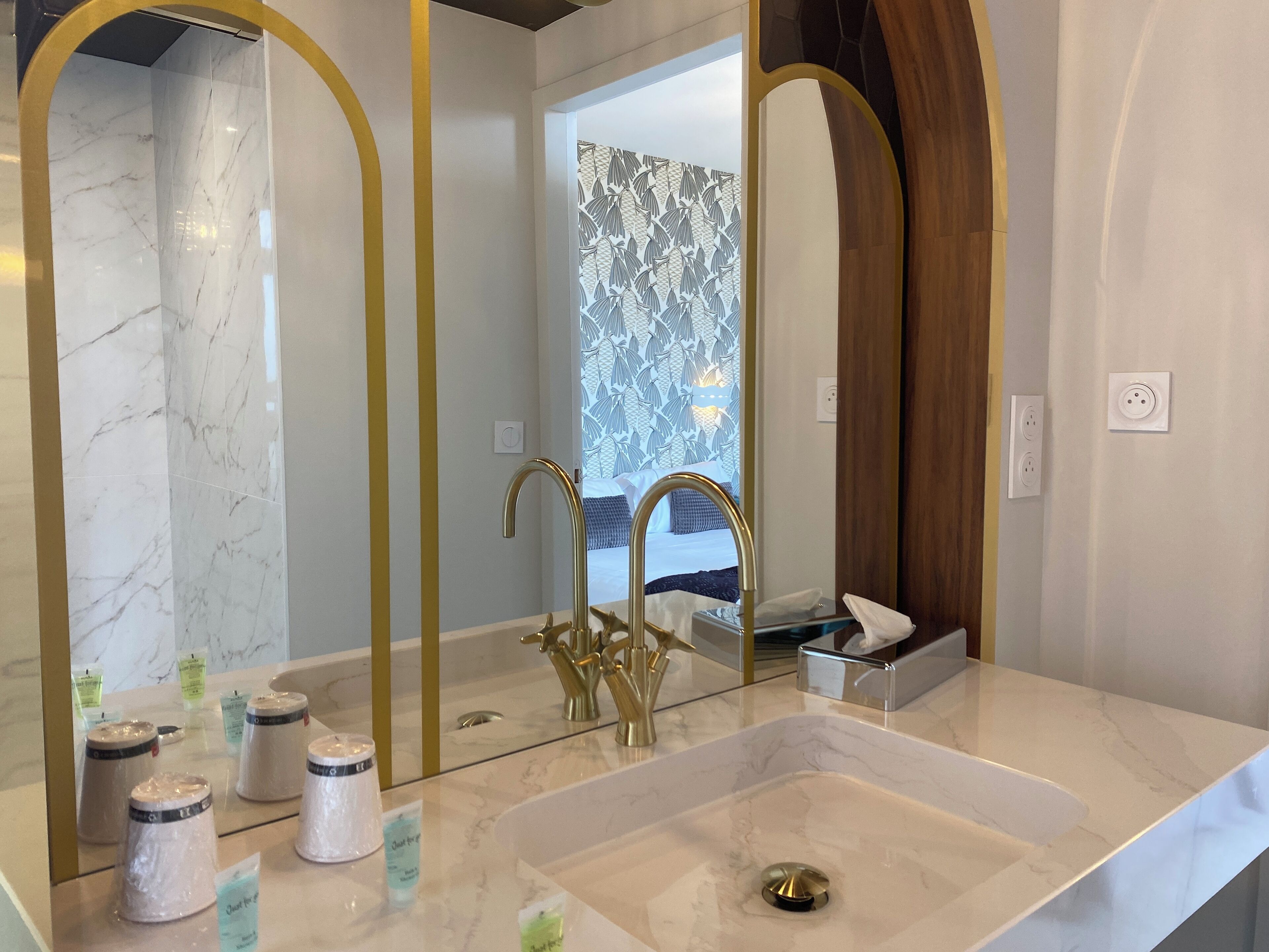 A modern bathroom with a marble sink, gold faucets, and a large mirror with gold arches.
