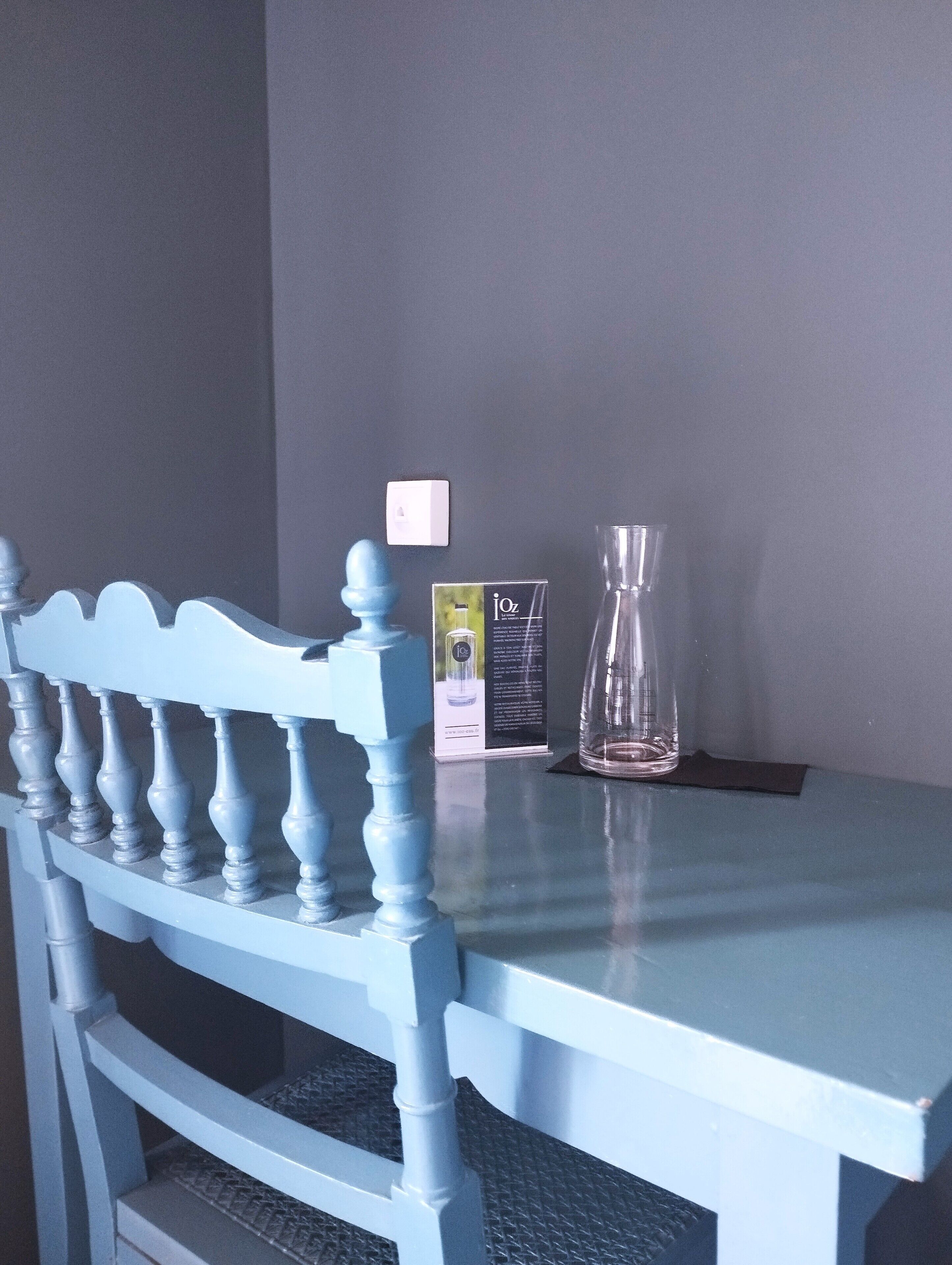A blue chair with a decorative backrest, a clear glass vase, and a small white switch on a grey wall.