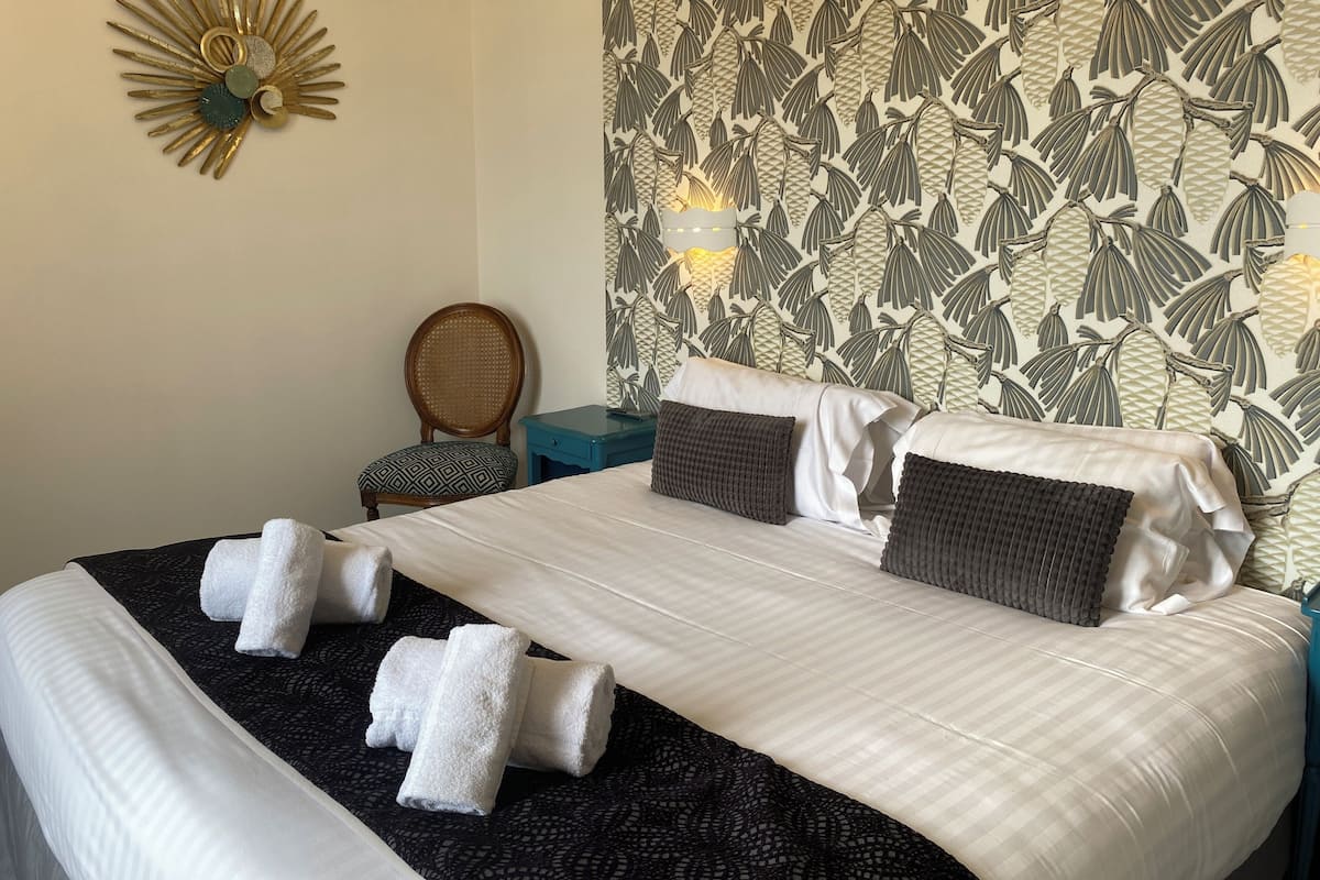 A hotel room with a large bed, two pillows, a chair, and a decorative wall piece.