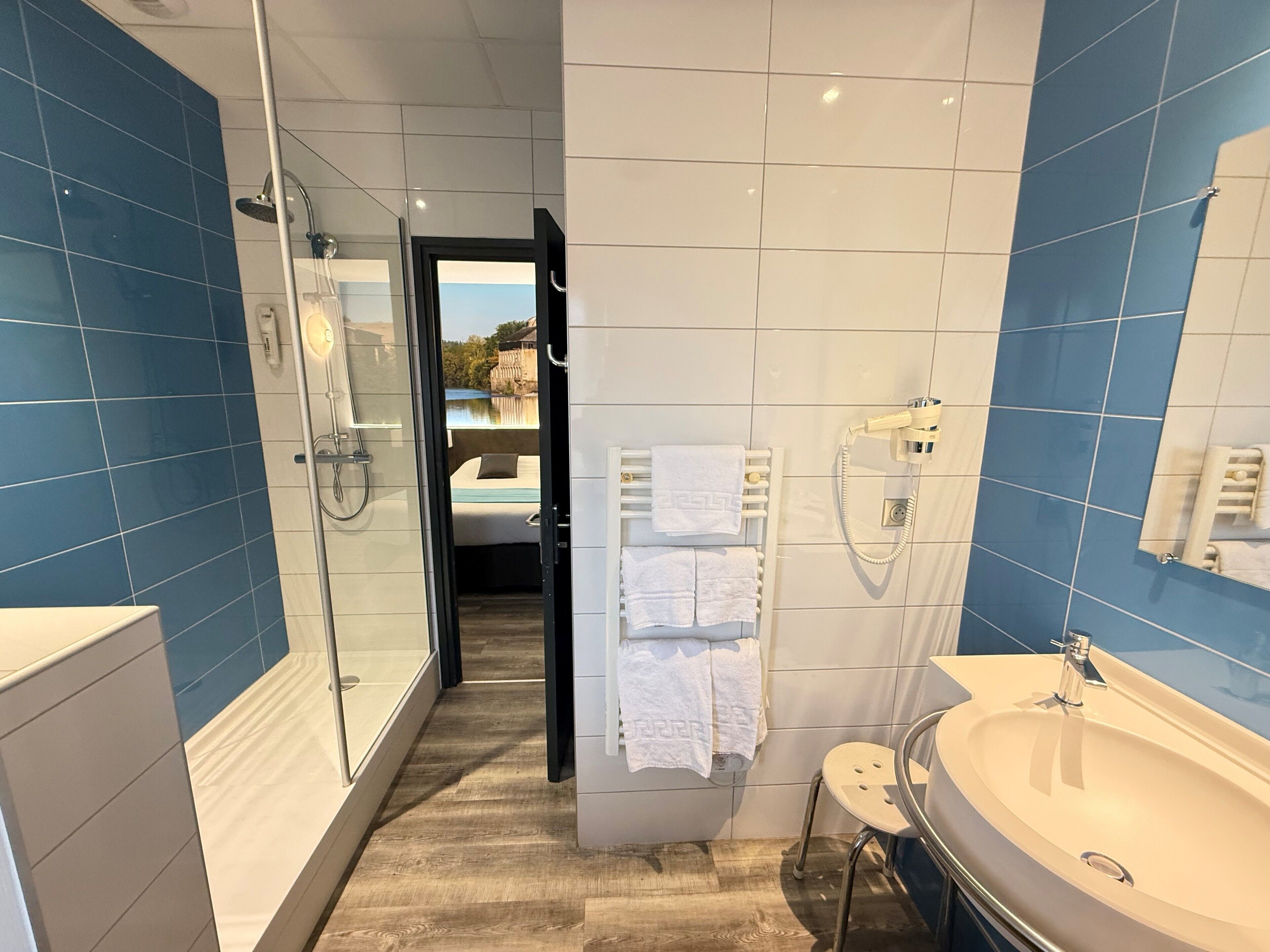 A modern bathroom with a glass shower, a large sink, and a view of a bedroom through an open door.