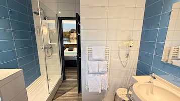 A modern bathroom with a glass shower, a large sink, and a view of a bedroom through an open door.