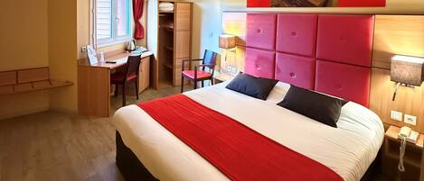 Ein Hotelzimmer mit einem großen Bett, einem Schreibtisch, einem Stuhl und einem Kleiderschrank.
